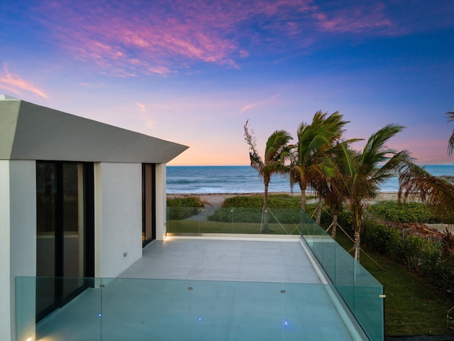 pool at dusk featuring a view of the beach and a water view