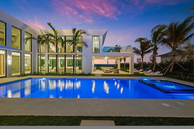 pool at dusk featuring an in ground hot tub, an outdoor hangout area, and a patio area