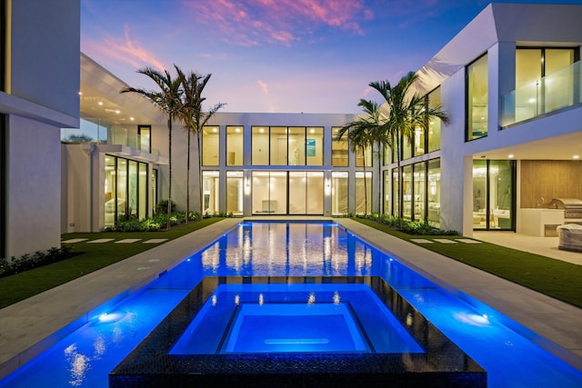 pool at dusk with exterior kitchen and an in ground hot tub