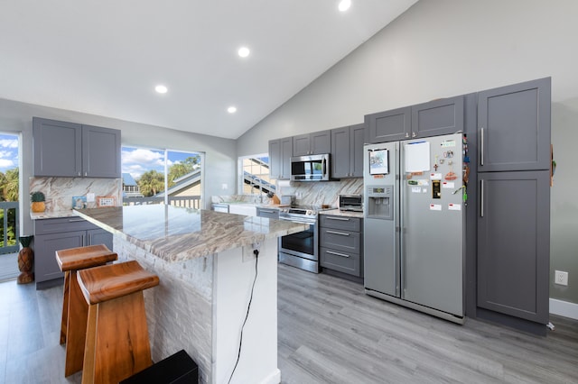 kitchen with light stone counters, light hardwood / wood-style flooring, gray cabinets, a kitchen island, and appliances with stainless steel finishes