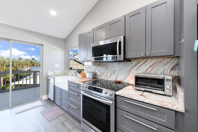 kitchen with appliances with stainless steel finishes, lofted ceiling, gray cabinetry, and light hardwood / wood-style flooring