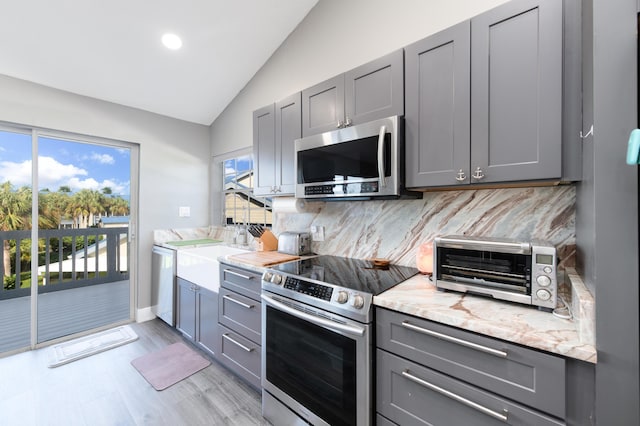 1441 NE 14th Ct Unit 4, Jensen Beach, FL 34957 - kitchen featuring appliances with stainless steel finishes, gray cabinets, lofted ceiling, tasteful backsplash, and light stone countertops