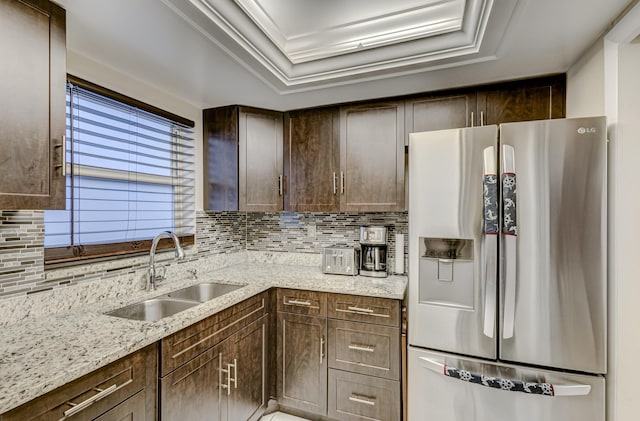 kitchen with sink, decorative backsplash, light stone counters, stainless steel refrigerator with ice dispenser, and dark brown cabinets