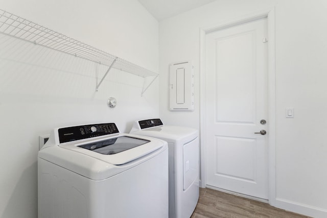 washroom with electric panel, light hardwood / wood-style floors, and washing machine and clothes dryer