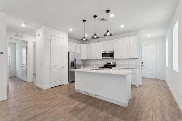 kitchen with white cabinets, stainless steel appliances, hanging light fixtures, and a center island with sink