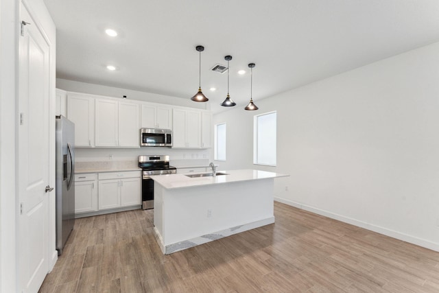 kitchen with white cabinets, an island with sink, appliances with stainless steel finishes, decorative light fixtures, and light hardwood / wood-style floors