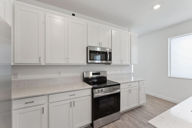 kitchen with white cabinets, light stone counters, light wood-type flooring, and appliances with stainless steel finishes