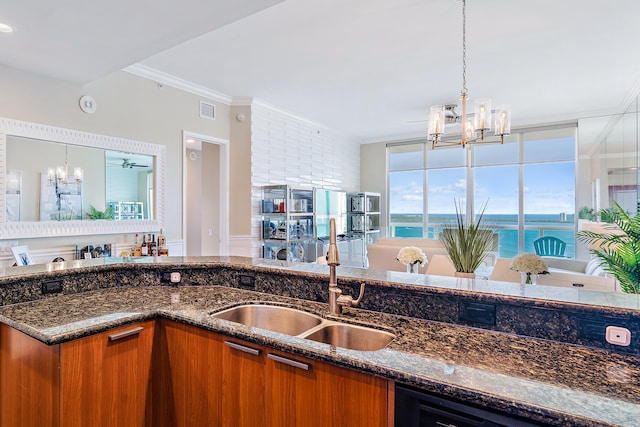 kitchen with crown molding, dark stone counters, hanging light fixtures, sink, and a water view