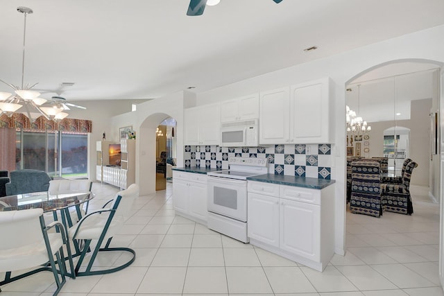 kitchen with arched walkways, dark countertops, white cabinets, white appliances, and ceiling fan with notable chandelier