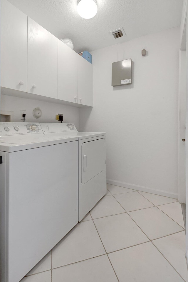 laundry area with a textured ceiling, light tile patterned flooring, visible vents, cabinet space, and washing machine and clothes dryer