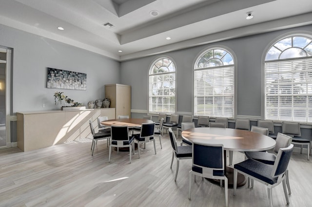 dining space featuring light wood-type flooring, a raised ceiling, visible vents, and wainscoting