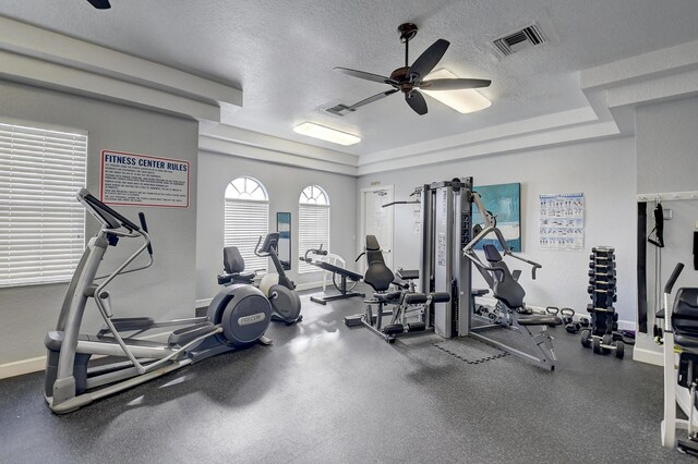 exercise room with a ceiling fan, a raised ceiling, visible vents, and baseboards