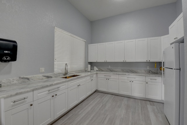 kitchen featuring light stone countertops, sink, white fridge, light hardwood / wood-style floors, and white cabinets