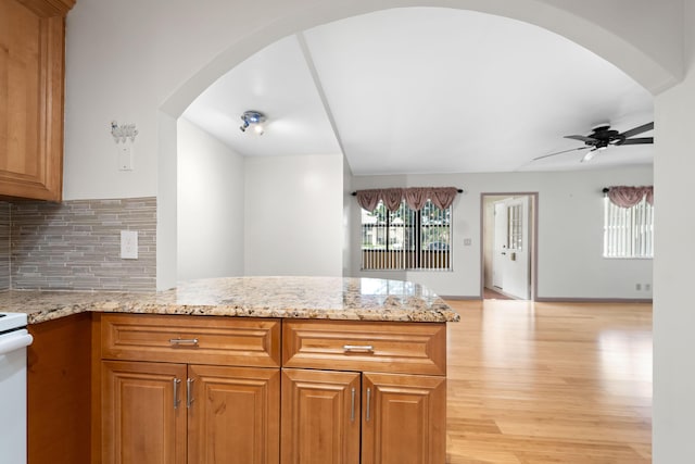 kitchen featuring ceiling fan, light stone countertops, kitchen peninsula, and tasteful backsplash