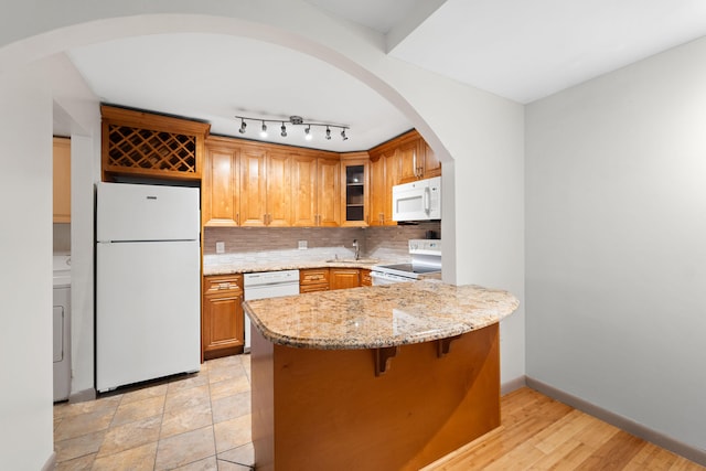 kitchen with white appliances, tasteful backsplash, light stone counters, kitchen peninsula, and washer / dryer