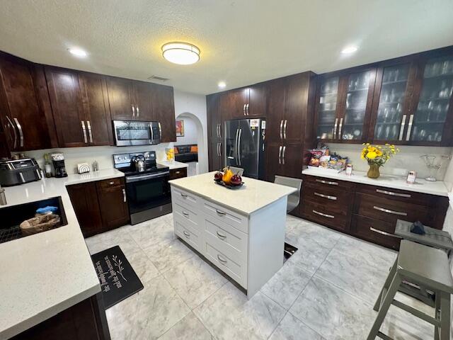 kitchen with dark brown cabinets, appliances with stainless steel finishes, a textured ceiling, and a kitchen island