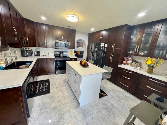 kitchen with a textured ceiling, appliances with stainless steel finishes, sink, and a kitchen island