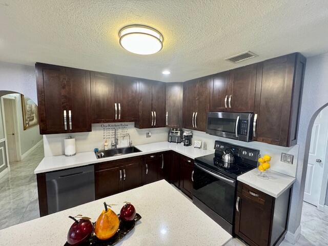 kitchen featuring sink, a textured ceiling, dark brown cabinets, and stainless steel appliances