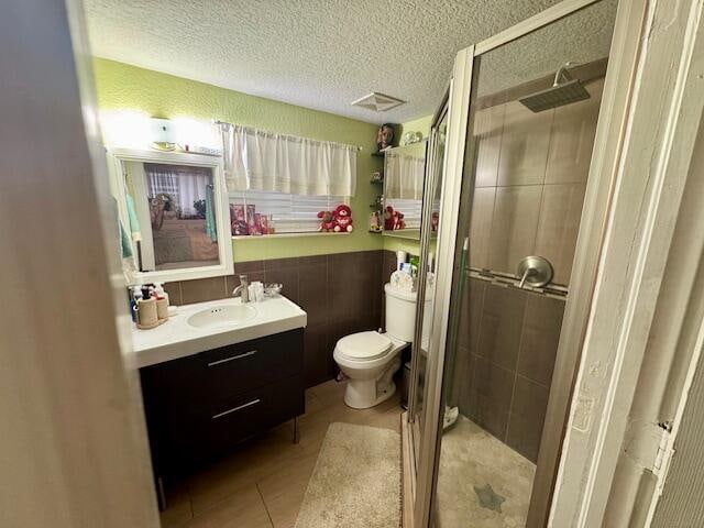 bathroom featuring a textured ceiling, vanity, a shower with shower door, tile patterned floors, and toilet