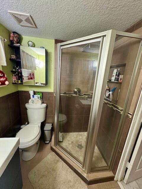 bathroom featuring walk in shower, a textured ceiling, vanity, toilet, and tile walls