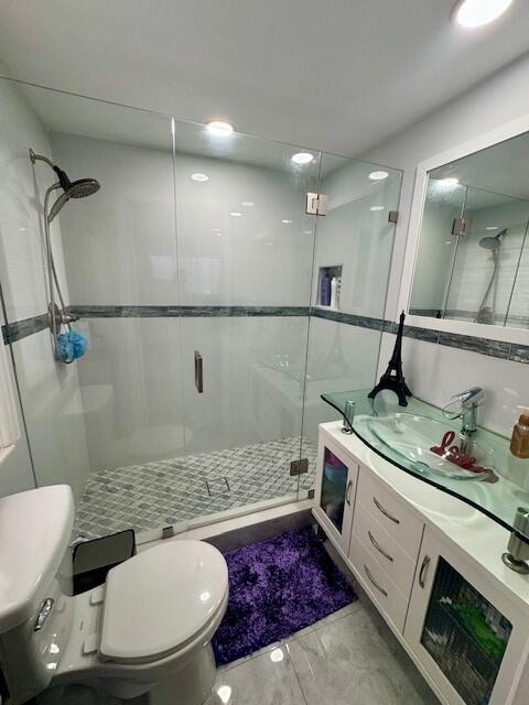 bathroom with a shower with shower door, vanity, and toilet