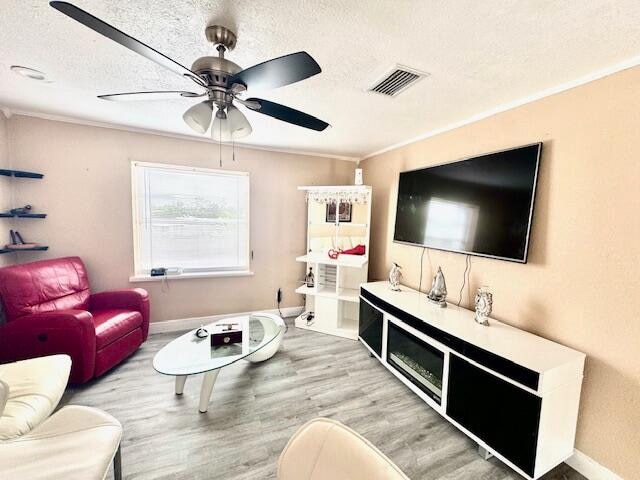 living room featuring ceiling fan, a textured ceiling, crown molding, and light hardwood / wood-style flooring