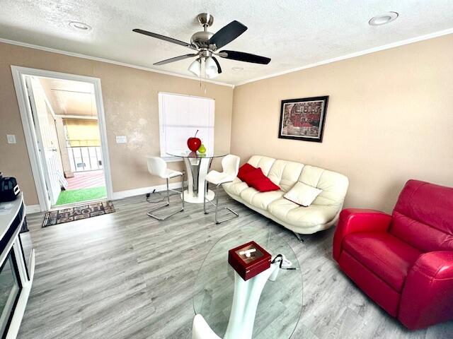 living room featuring a textured ceiling, hardwood / wood-style flooring, ceiling fan, and crown molding