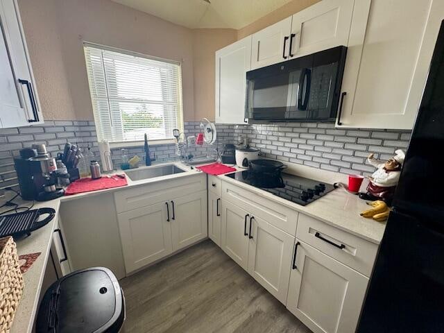 kitchen with white cabinets, light wood-type flooring, black appliances, and tasteful backsplash