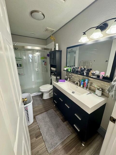 bathroom with wood-type flooring, toilet, a shower with door, tasteful backsplash, and vanity