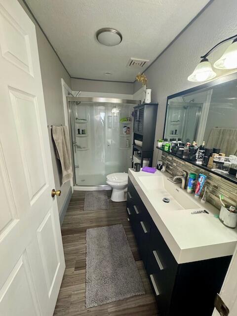 bathroom featuring wood-type flooring, a shower with door, backsplash, vanity, and toilet