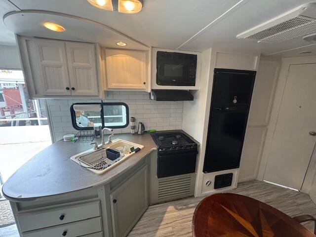 kitchen with black appliances, tasteful backsplash, ventilation hood, sink, and light hardwood / wood-style flooring