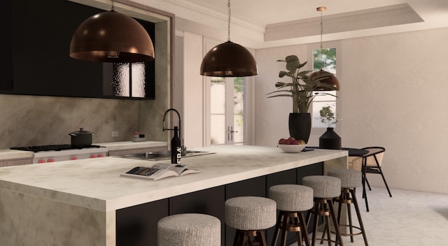 kitchen with a kitchen bar, sink, ornamental molding, a tray ceiling, and decorative light fixtures