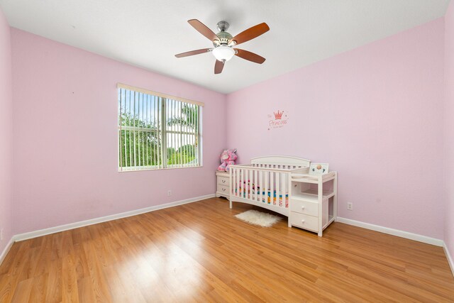 bedroom featuring hardwood / wood-style floors, ceiling fan, and a nursery area