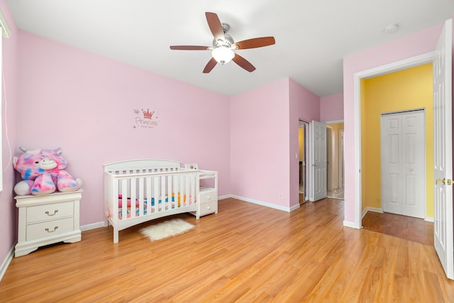 bedroom featuring a crib, ceiling fan, a closet, and light wood-type flooring