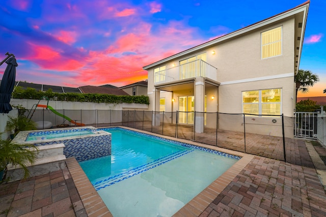 pool at dusk with a patio and an in ground hot tub