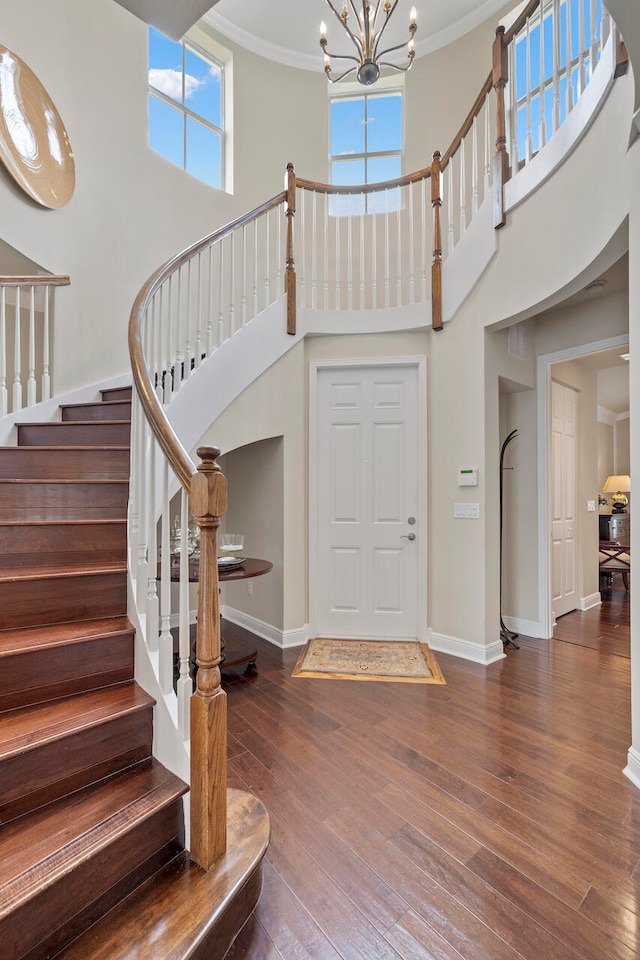 entrance foyer with a towering ceiling, dark wood-type flooring, a chandelier, and crown molding