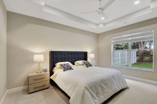 bedroom with a raised ceiling, light carpet, and ceiling fan