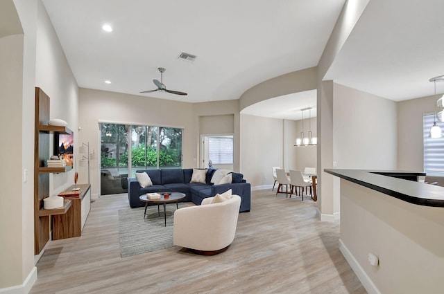 living room featuring ceiling fan with notable chandelier and light wood-type flooring