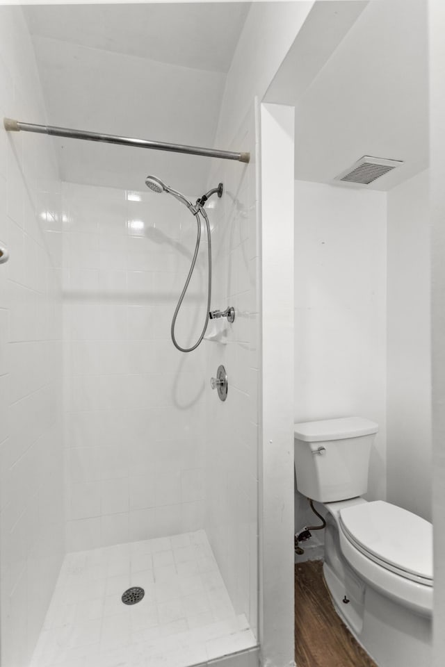 bathroom with a tile shower, hardwood / wood-style floors, and toilet