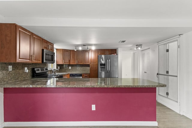 kitchen featuring appliances with stainless steel finishes, backsplash, light wood-type flooring, and kitchen peninsula