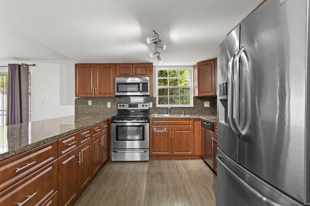 kitchen with sink, appliances with stainless steel finishes, dark stone counters, light hardwood / wood-style floors, and backsplash