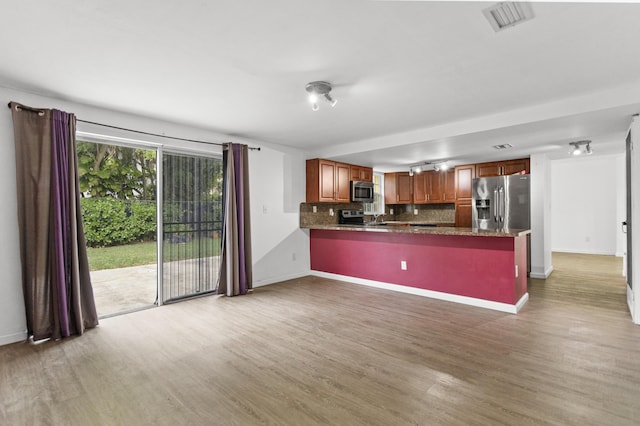 kitchen featuring light hardwood / wood-style flooring, dark stone countertops, kitchen peninsula, stainless steel appliances, and decorative backsplash