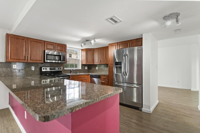 kitchen with sink, appliances with stainless steel finishes, backsplash, wood-type flooring, and dark stone counters