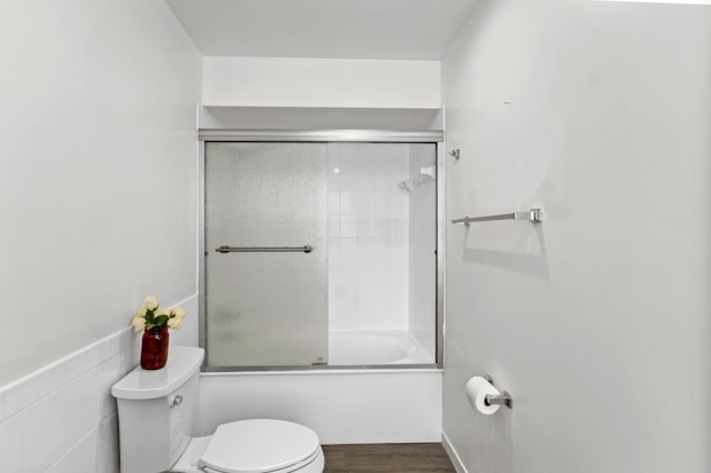 bathroom featuring tile walls, wood-type flooring, bath / shower combo with glass door, and toilet