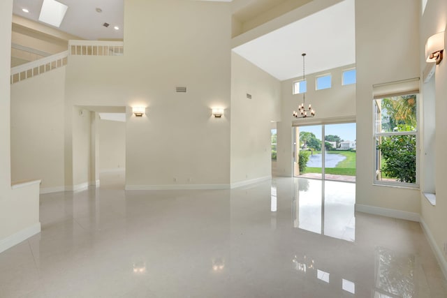 tiled spare room featuring a high ceiling, a chandelier, and a skylight