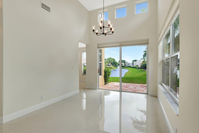 doorway to outside with a water view, a chandelier, light tile patterned flooring, and a towering ceiling