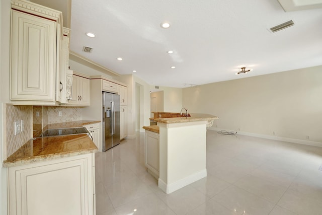 kitchen featuring cream cabinets, a kitchen island, stainless steel fridge with ice dispenser, light stone countertops, and decorative backsplash