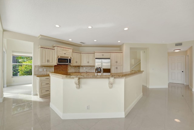 kitchen with light stone countertops, cream cabinetry, light tile patterned floors, and appliances with stainless steel finishes