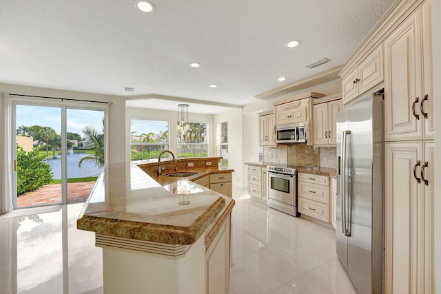 kitchen with sink, a kitchen island with sink, backsplash, appliances with stainless steel finishes, and cream cabinetry