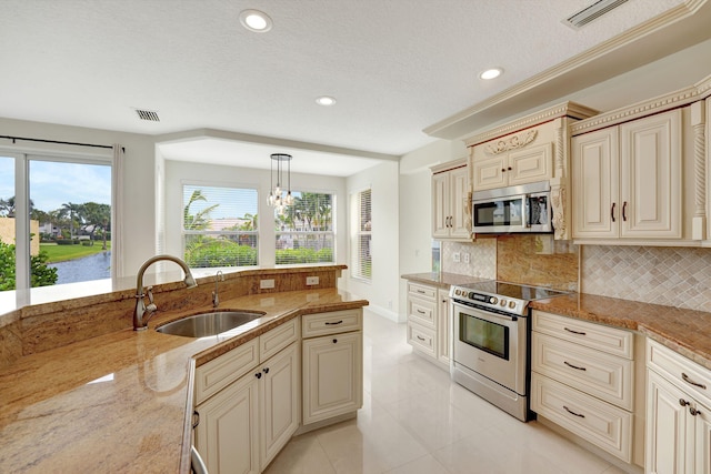 kitchen featuring light stone counters, stainless steel appliances, pendant lighting, sink, and cream cabinetry